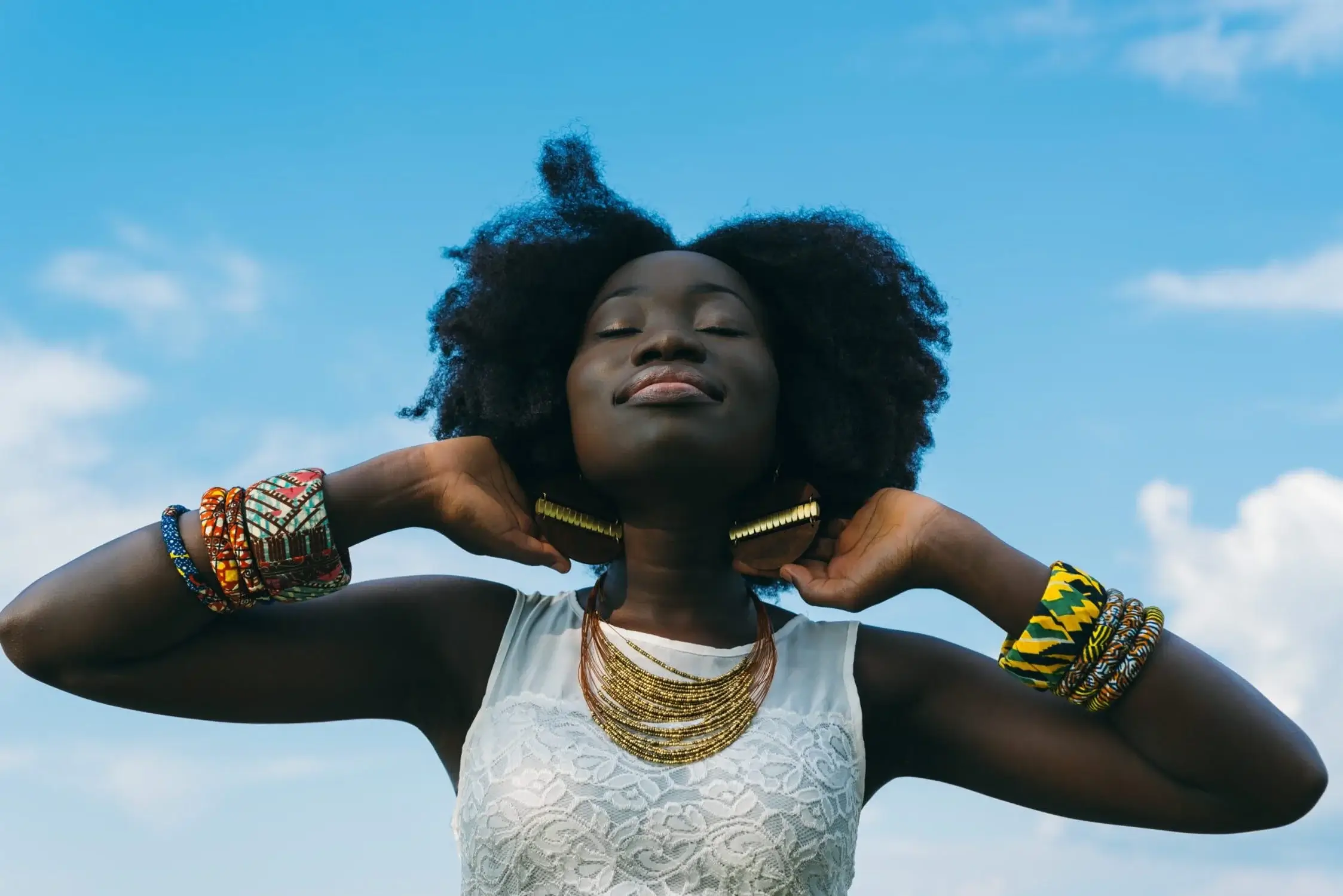 Woman wearing gold jewelry and colorful bracelets against a blue sky, fashion accessories and personal